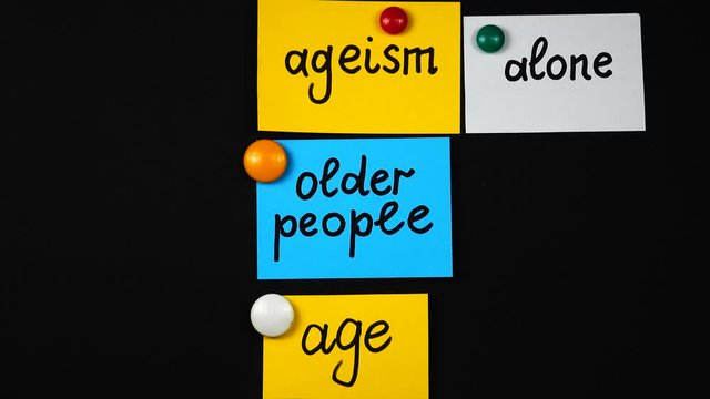 Lecturer places on magnetic board sheets of paper with the terms related to ageism at a lecture on the problem of ageism. Using of a visual aids