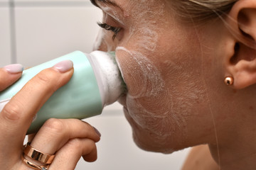 Girl is cleaning face with electric brush. Woman with special brush for deep cleansing facial...