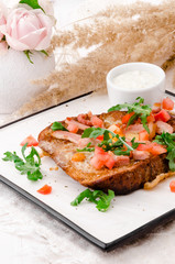 Fresh healthy breakfast. Dark toasts with fried eggs, slightly salted salmon and arugula on  white plate on light wooden background. Pink roses on the background. Close-up. Space