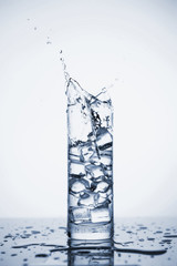 Clear mineral water splashes in a glass with ice.