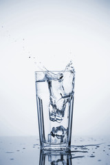 Clear mineral water splashes in a glass with ice.