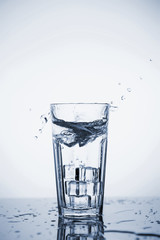 Clear mineral water splashes in a glass with ice.