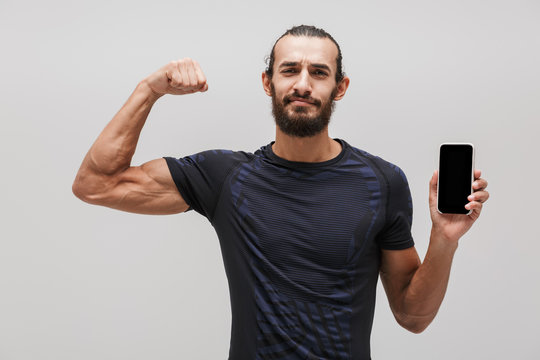 Image of muscular sportsman showing his bicep and holding smartphone