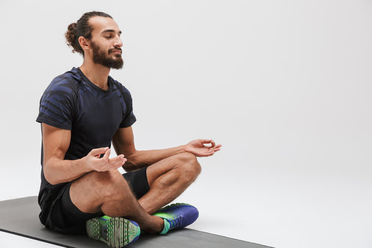 Image of sportsman in tracksuit meditating while sitting on yoga mat