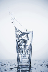 Clear mineral water splashes in a glass with ice.