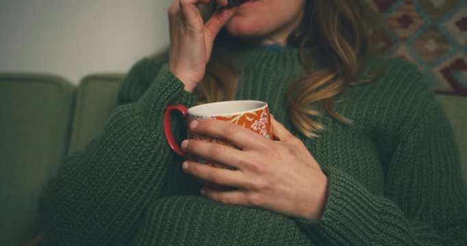 Woman drinking coffe and eating chocolate on sofa
