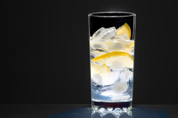 glass cup with water, ice cubes and lemon on a dark background