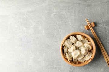 Chopsticks and bowl with dumplings on grey background, space for text