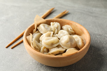 Chopsticks and bowl with dumplings on grey background, close up