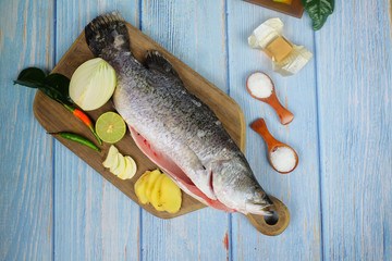 Wooden cutting board   with baramundi, salt, msg,ginger,garlic,onion,key lime, chilies,  and...