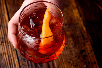 Man with an abstract tattoo on his hand is holding a faceted glass with the Negroni alcoholic drink