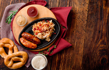 Glass of dark beer with foam and fried sausages with cranberry-honey stewed cabbage served in cast-iron pan