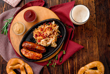 Glass of dark beer with foam and fried sausages with cranberry-honey stewed cabbage served in cast-iron pan
