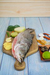 Wooden cutting board   with baramundi, salt, msg,ginger,garlic,onion,key lime, chilies,  and lemongrass over the wooden background.