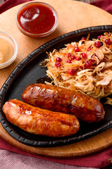 Fried sausages with cranberry-honey stewed cabbage served in cast-iron pan on round wooden board