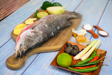 Wooden cutting board   with baramundi, salt, msg,ginger,garlic,onion,key lime, chilies,  and lemongrass over the wooden background.
