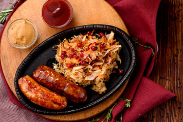 Fried sausages with cranberry-honey stewed cabbage served in cast-iron pan on round wooden board