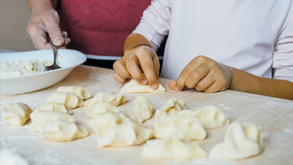 Grandmother with granddaughter is making dumplings with cheese at home kitchen together