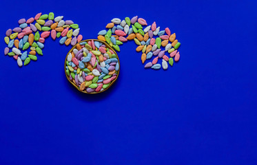 Sunflower seeds in colored glaze on a blue background laid out in the form of a rabbit. Easter, flat lay, copy space, top view.