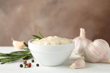 Bowl of garlic sauce, ingredients on white table against brown background, space for text. Closeup