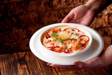 Baked salmon in a creamy sauce with tomatoes in a white plate on a dark wooden background