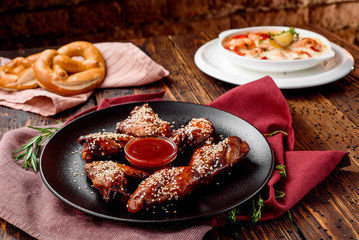 Beautiful fried chicken wings sprinkled with white sesame seeds on black matte plate, served with red barbecue sauce