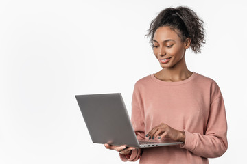 Smiling woman in casual clothes holding laptop and sending email standing over white background