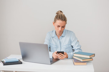 Young serious caucasian girl student communicates in social networks while preparing for exams while sitting at table with notebook books and laptop. Charming businesswoman makes an informal meeting