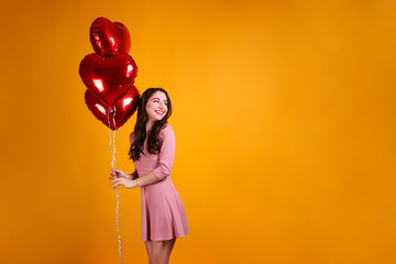 Portrait of young brunette woman posing with helium inflated air balloon. Happy valentine's day concept. Joyful female with wavy hair over colorful background. Close up, copy space for text.