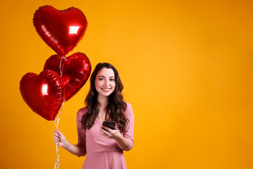 Portrait of young brunette woman posing with helium inflated air balloon. Happy valentine's day concept. Joyful female with wavy hair over colorful background. Close up, copy space for text.