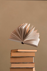 an open book levitating above stack of books	on beige background