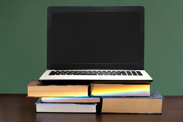 white and black laptop on stack of books on a dark wooden table