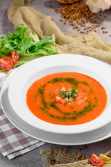 Spanish cold gazpacho puree soup in a white plate on a light concrete background in a beautiful composition with fresh vegetables and light napkins. Close-up. Space
