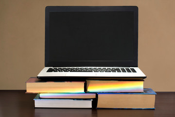 white and black laptop on stack of books on a dark wooden table
