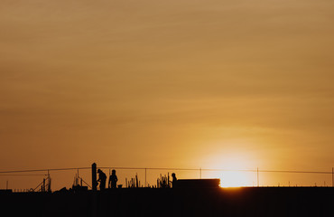 Obraz premium Silhouette sunset construction working and machinery crane hoisting cement mortar mixer bucket container in construction site