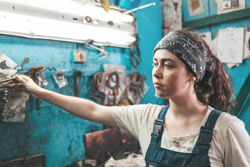 Gender equality. A portrait of a young woman in uniform working in a workshop, taking tools from a tool box on the wall and looking away