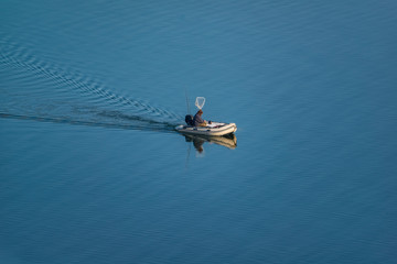 Fisherman in the middle of blue lake fishing on a rubber inflatable motor boat.