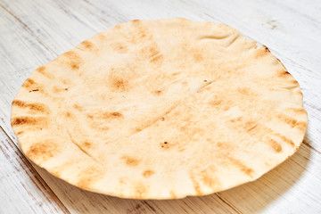 round pita bread on a light wooden background.