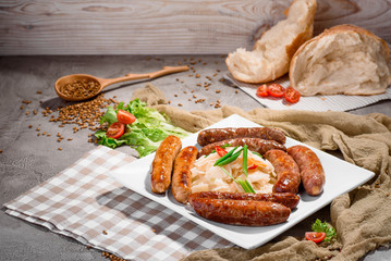 Beer snack. Four types of grilled sausages with sauerkraut and greens on white plate on concrete background, decorated with checkered napkin and fresh vegetables. Close-up. Space