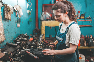 Gender equality. Portrait of a young brunette woman in uniform who works with a hammer in her hand. Blue wall and spare parts in the background