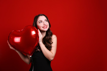 Portrait of young brunette woman posing with helium inflated air balloon. Happy valentine's day concept. Joyful female with wavy hair over colorful background. Close up, copy space for text.