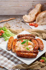 Beer snack. Four types of grilled sausages with sauerkraut and greens on white plate on concrete background, decorated with checkered napkin and fresh vegetables. Close-up. Space