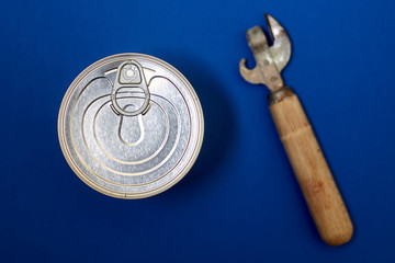 Canned food with a key for opening and an old can opener on a blue background.