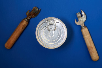 Canned food with a key for opening and an old can opener on a blue background.