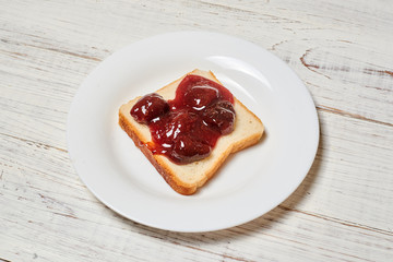 Toast with strawberry jam on a white plate on a light wooden background.
