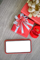 White blank screen of phone with gift boxes and ring on wooden background.