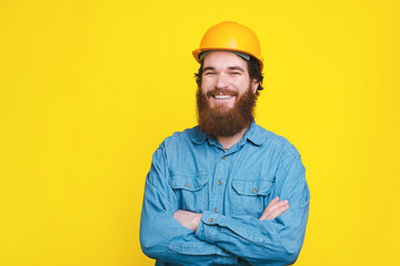 Portrait of happy young architect with crossed arms standing over yellow background