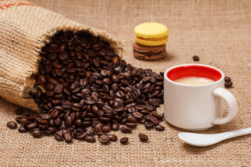 Cup of coffee and roasted coffee beans in a canvas sack.