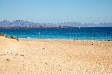 View on sand dune beach from Vuerteventura with Lanzarote and Lobos canary island in the background - golden  yellow sand dunes light blue sky summer season holiday travel vacation seascape mountains