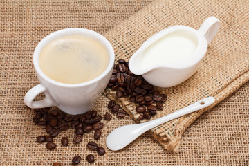 Cup of coffee, cream and coffee beans on sackcloth
